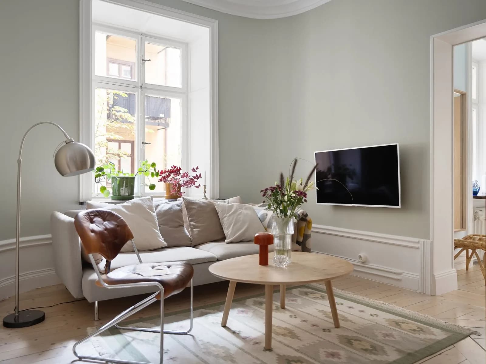 Minimalist living room with a white sofa, round wooden coffee table, plants, and natural light.