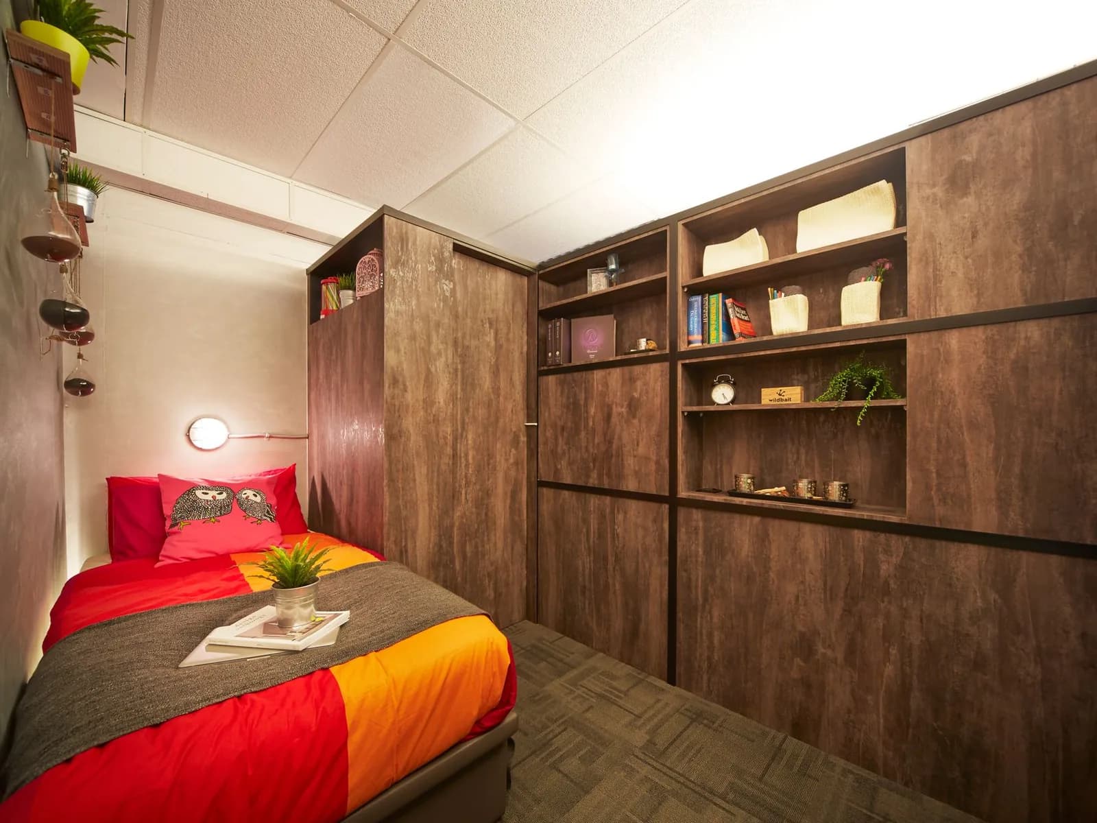 Compact bedroom with a single bed, tall wooden cupboards, and shelves that use the wall for storage.