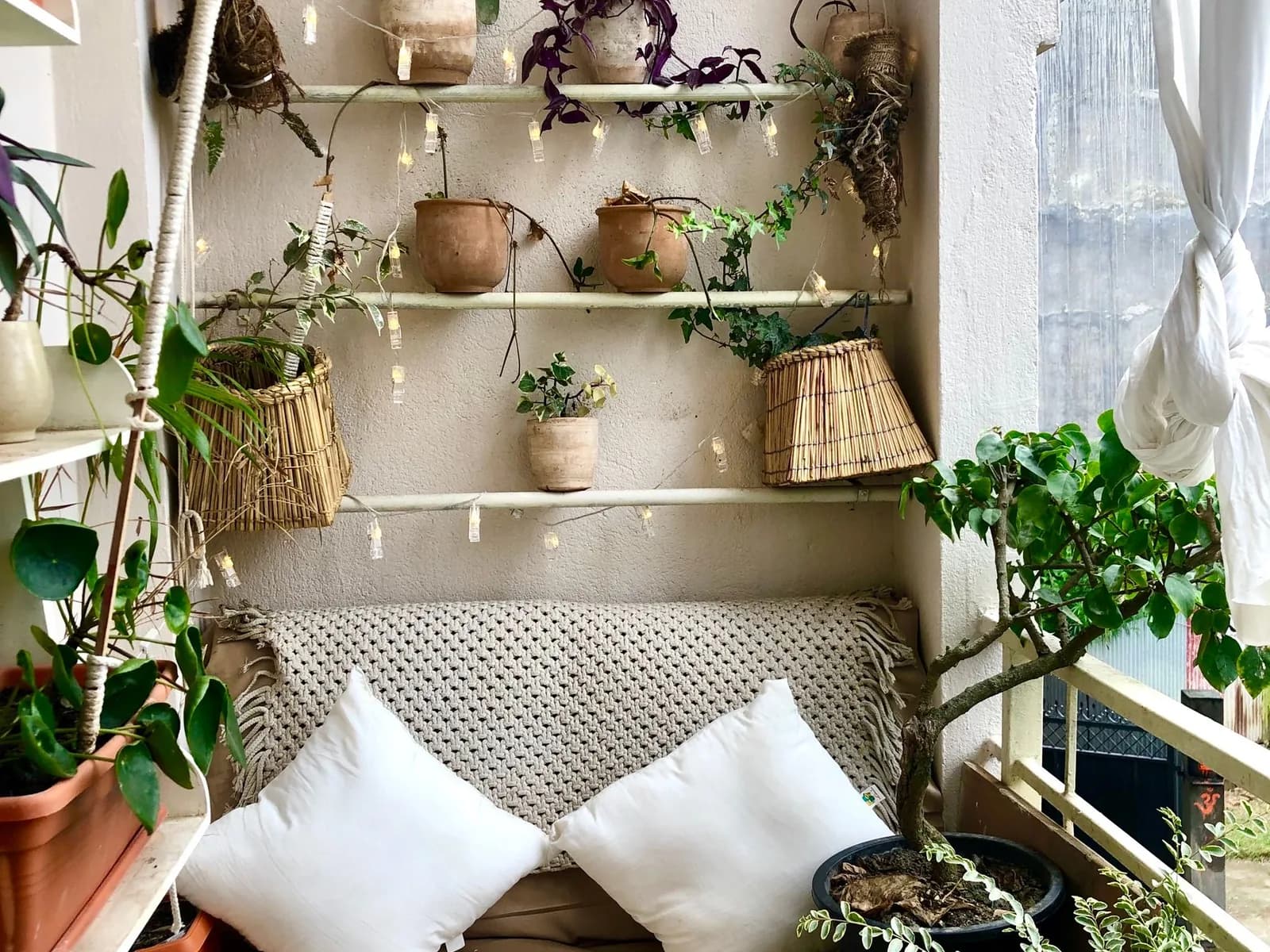 Balcony seating nook surrounded by potted plants, trailing greenery, and wall-mounted plant shelves.