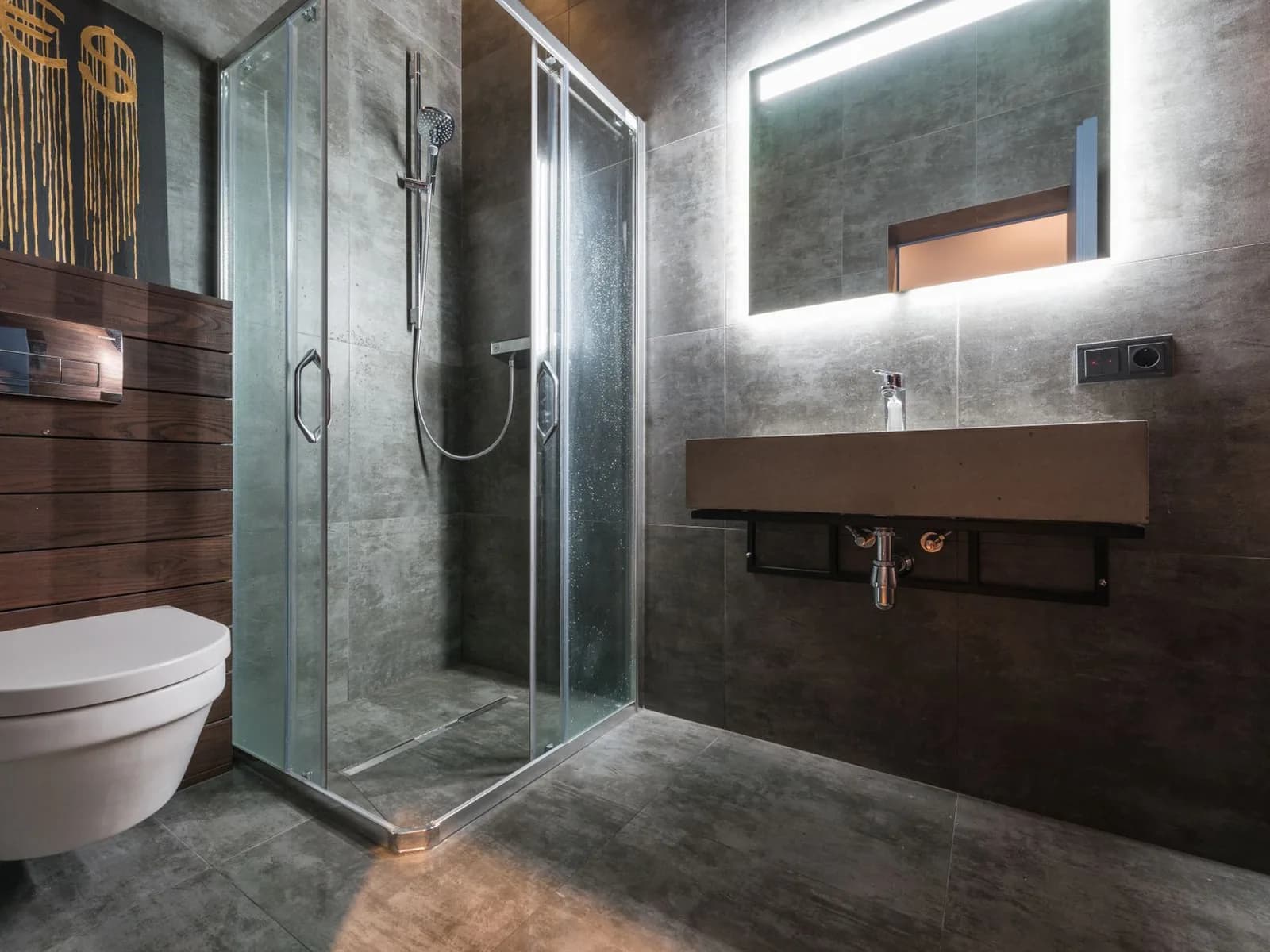 Modern bathroom with a glass shower enclosure, grey wall tiles, floating vanity, and illuminated mirror.