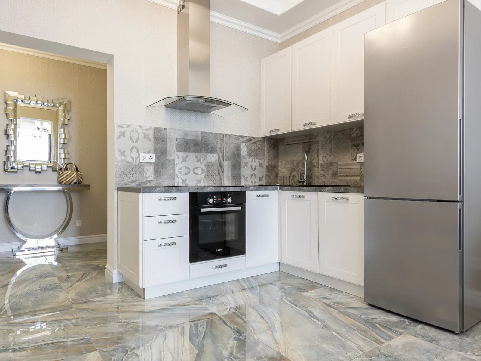 L-shaped kitchen with fitted white cabinets, a patterned tile backsplash, built-in oven, and stainless steel refrigerator.